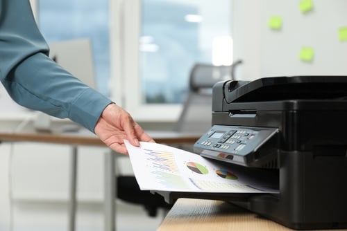 Er is een hand te zien die een afgedrukt document uit de printer haalt.