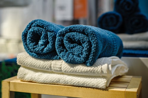 Vier schone zachte dubbele badhanddoeken in verschillende kleuren op elkaar gestapeld, liggend op een houten stoel.
